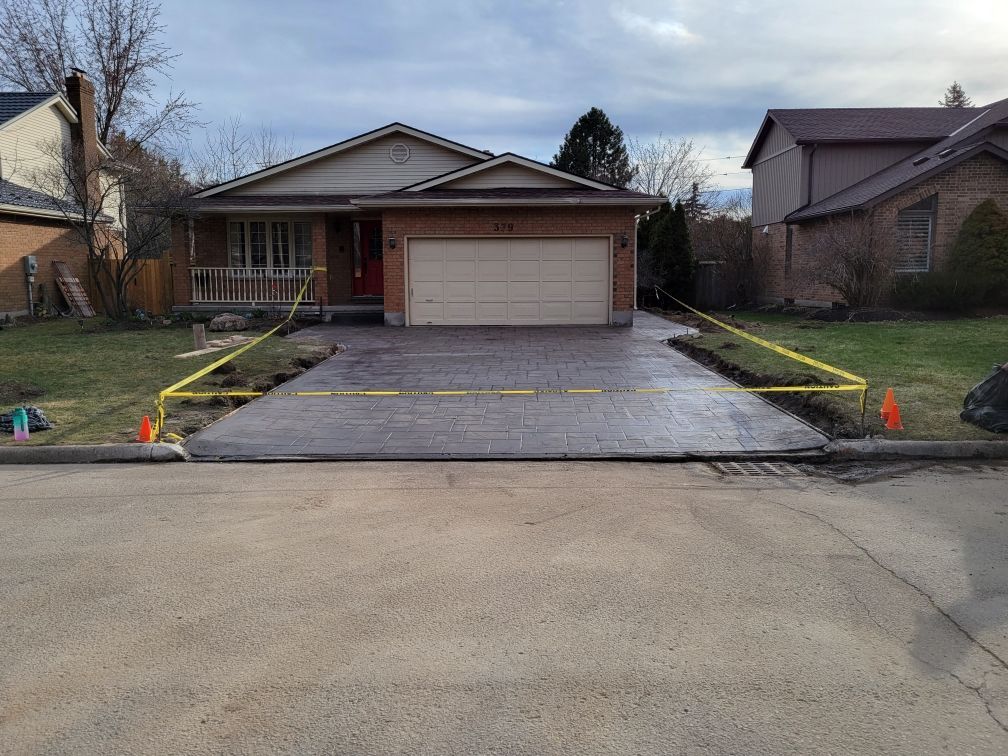 House front with newly paved driveway, cone markers, and a garage in a suburban neighborhood