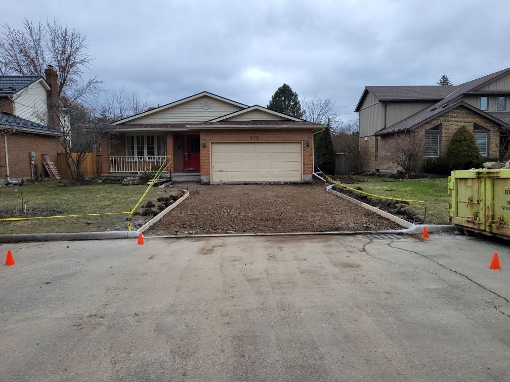 Gravel driveway under construction in front of a suburban house, marked by orange cones.