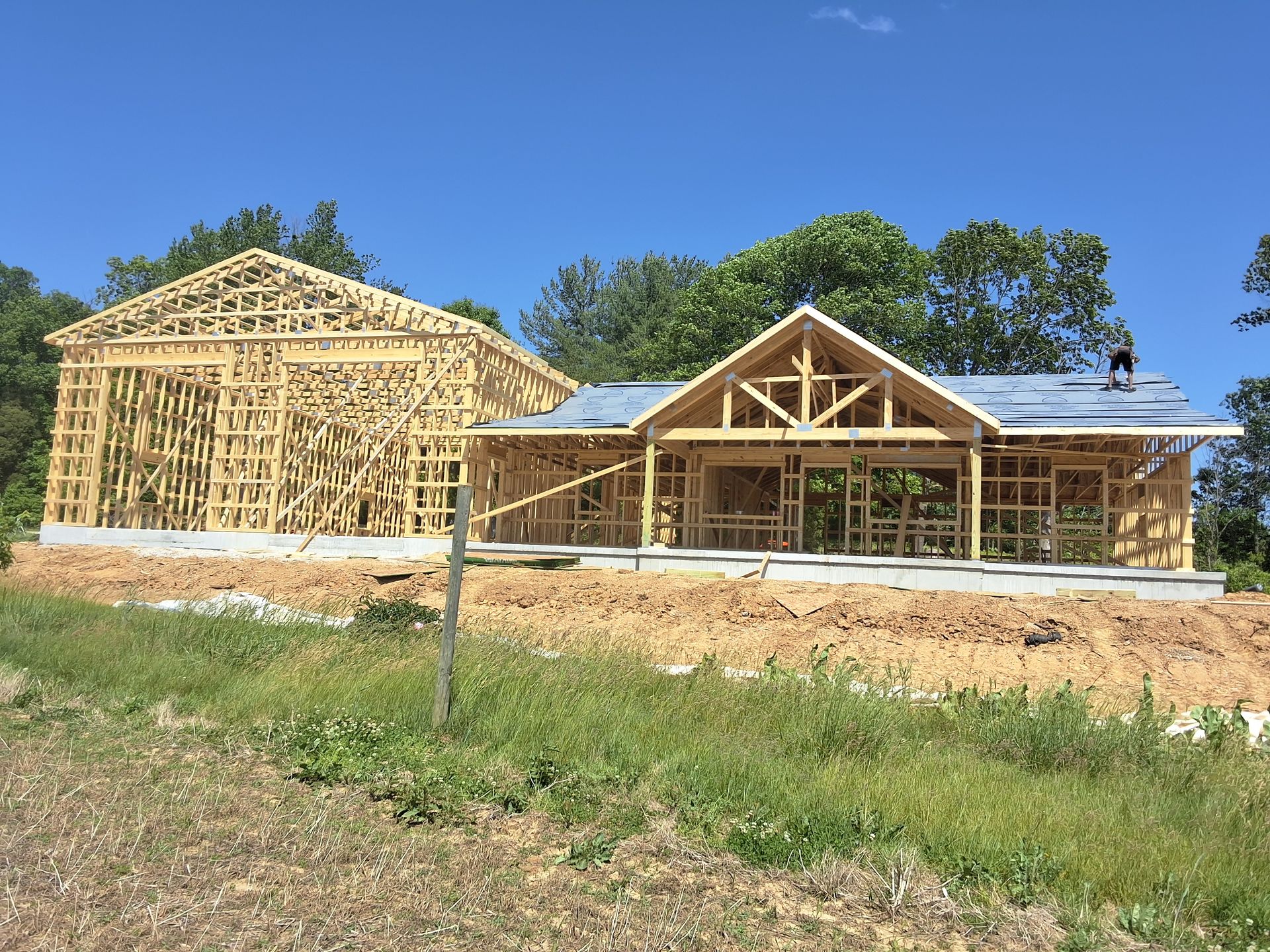 Partially built wooden house frames on a grassy lot under a clear blue sky