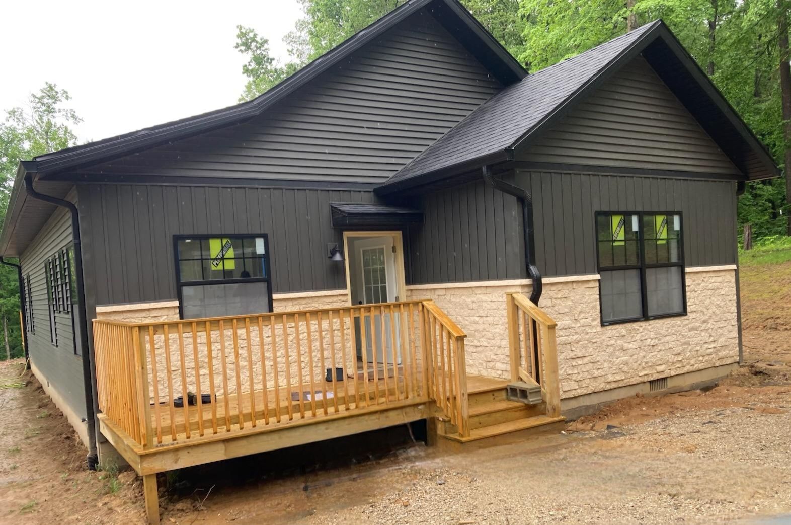 Small black house with a wooden front porch and tan stone base in a wooded area