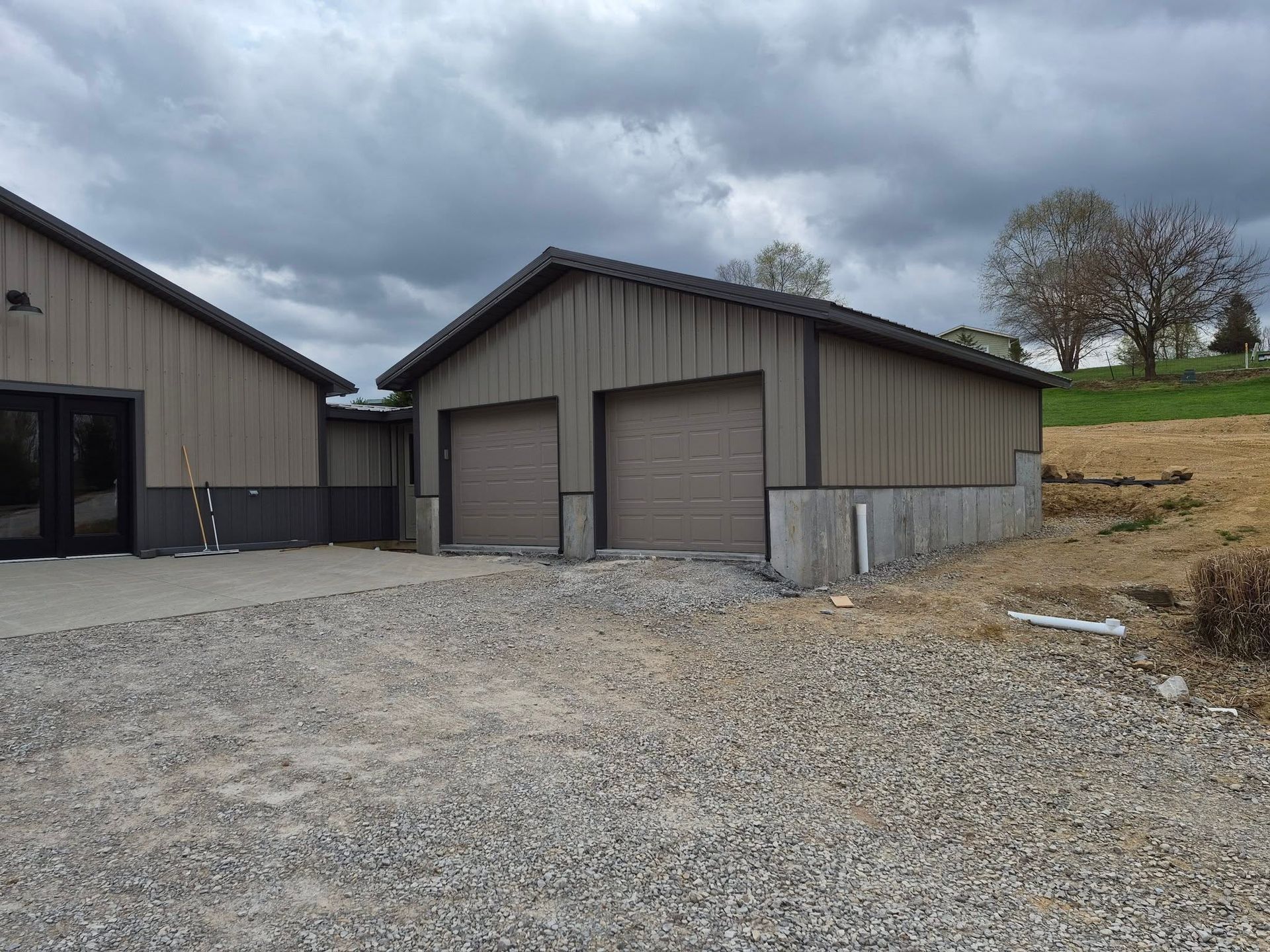 Gravel driveway beside a metal garage and barn under cloudy skies on a rural property