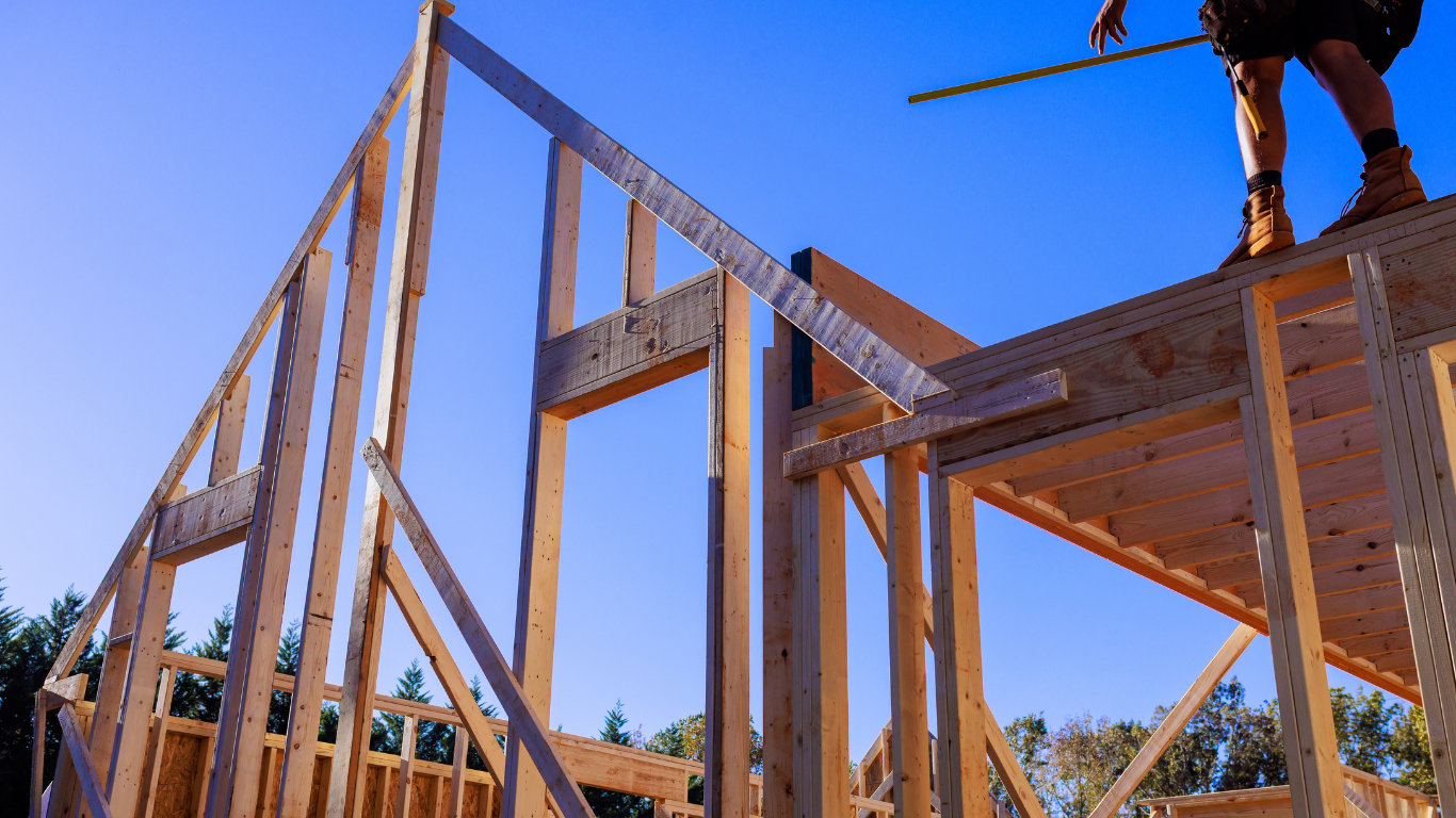 Wood-framed house under construction with workers on the roof against a blue sky