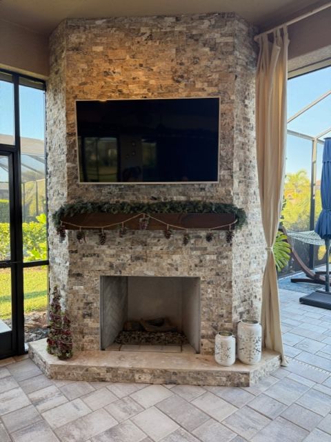 Stone fireplace with mounted TV and mantel in a bright room with tiled floor and windows