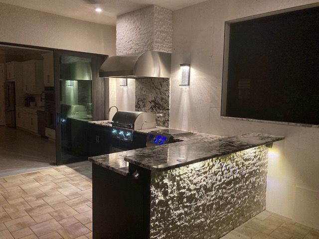 Modern kitchen with stone countertops, built-in grill, and large dark wall-mounted TV under warm lighting