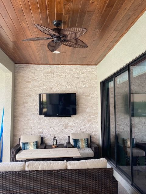 Covered patio with wicker seating, wall-mounted TV, ceiling fan, and sliding glass doors