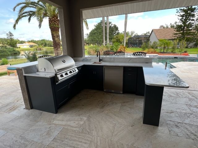 Modern outdoor kitchen with built-in grill and black cabinets under a covered patio by a pool