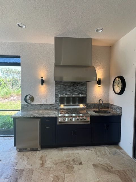Modern kitchen with stainless steel range hood, dark cabinets, marble countertop, and stone backsplash.