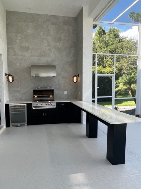 Modern outdoor kitchen with grill, black cabinets, concrete counter, and poolside view