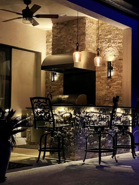 Elegant outdoor patio bar with ornate chairs, hanging lights, and a stone fireplace at dusk