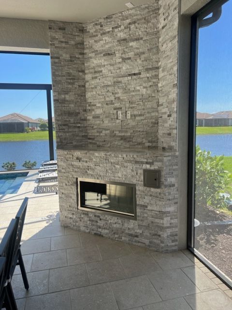 Covered patio with stone fireplace overlooking a lake and houses in the distance