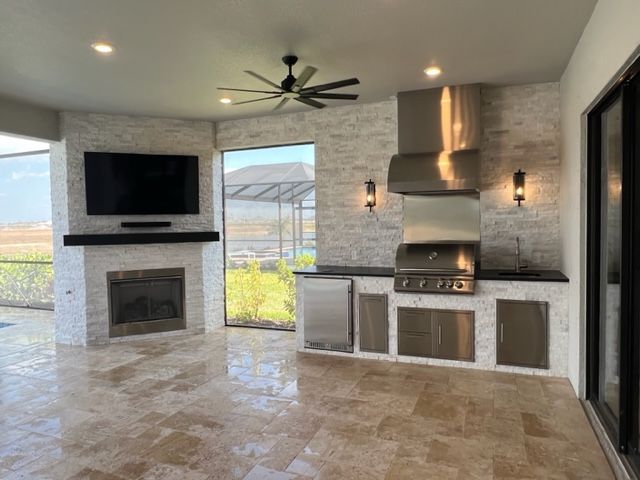 Modern outdoor covered patio with fireplace, TV, ceiling fan, and built-in grill and cabinets