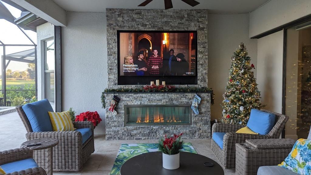 Patio lounge with stone fireplace, TV, Christmas tree, and wicker chairs with blue cushions
