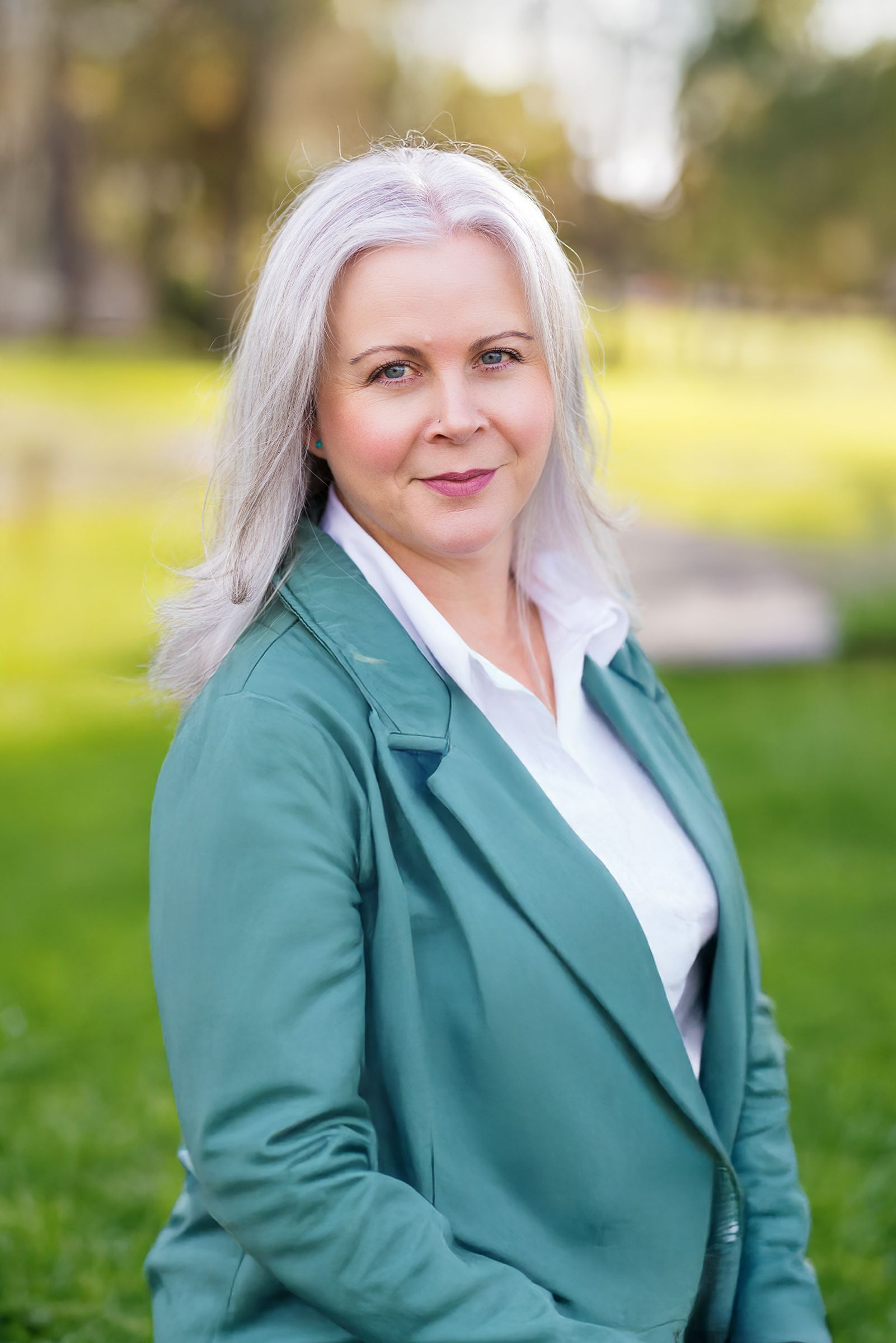 A woman in a black jacket is standing in front of a tree.