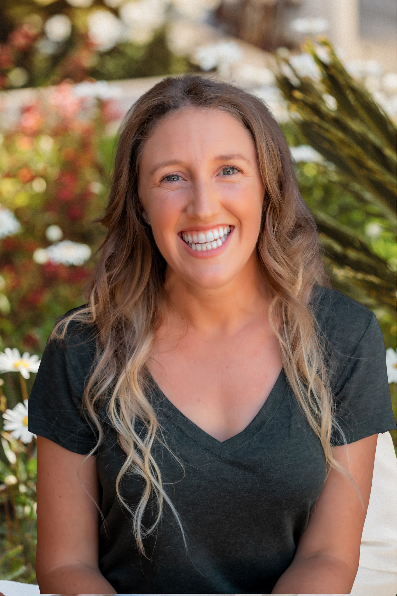 A woman is smiling for the camera while sitting on a bench in front of flowers.