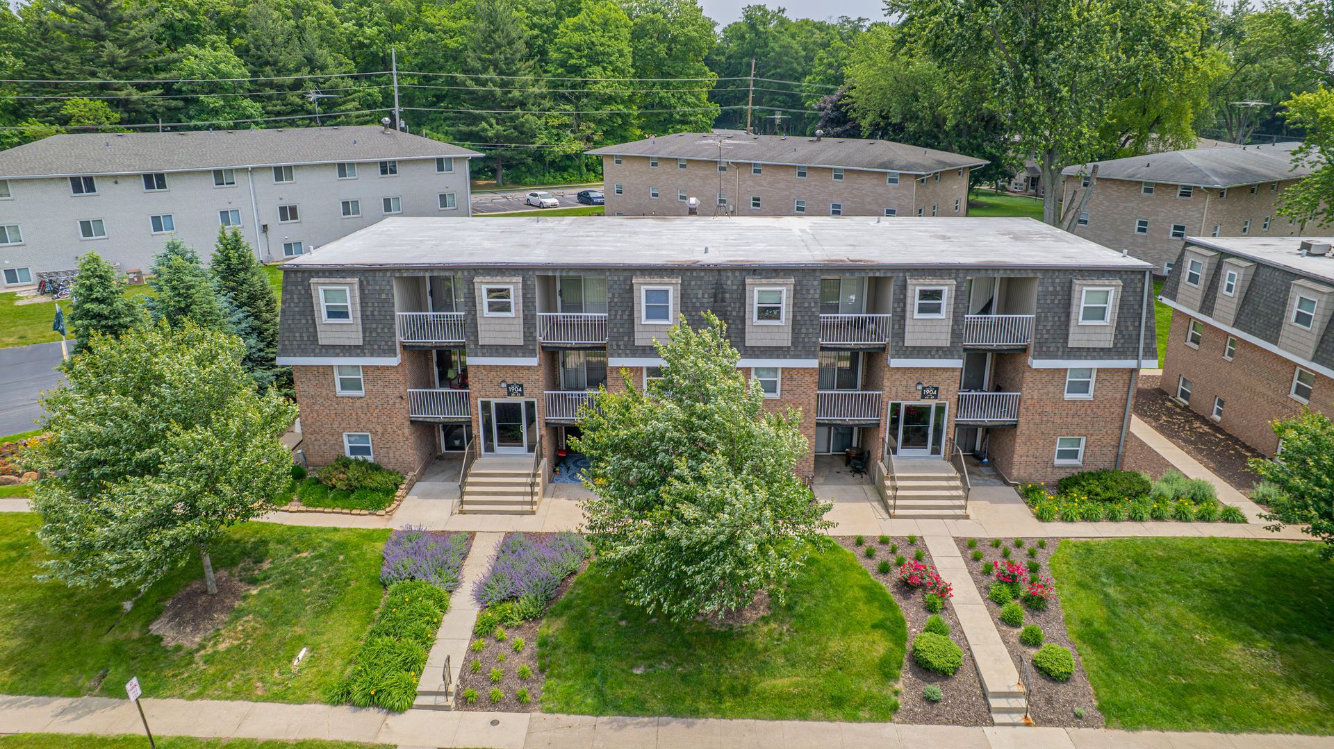 Two-story brick apartment buildings with gray roof, entry stairs, and landscaping.