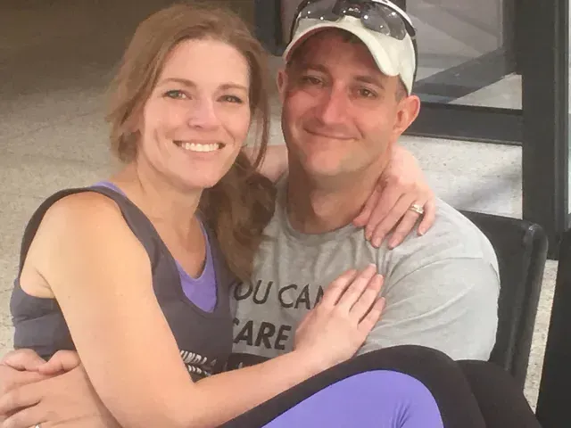 Smiling couple sitting together indoors, the woman holding a man’s shoulder and leg.