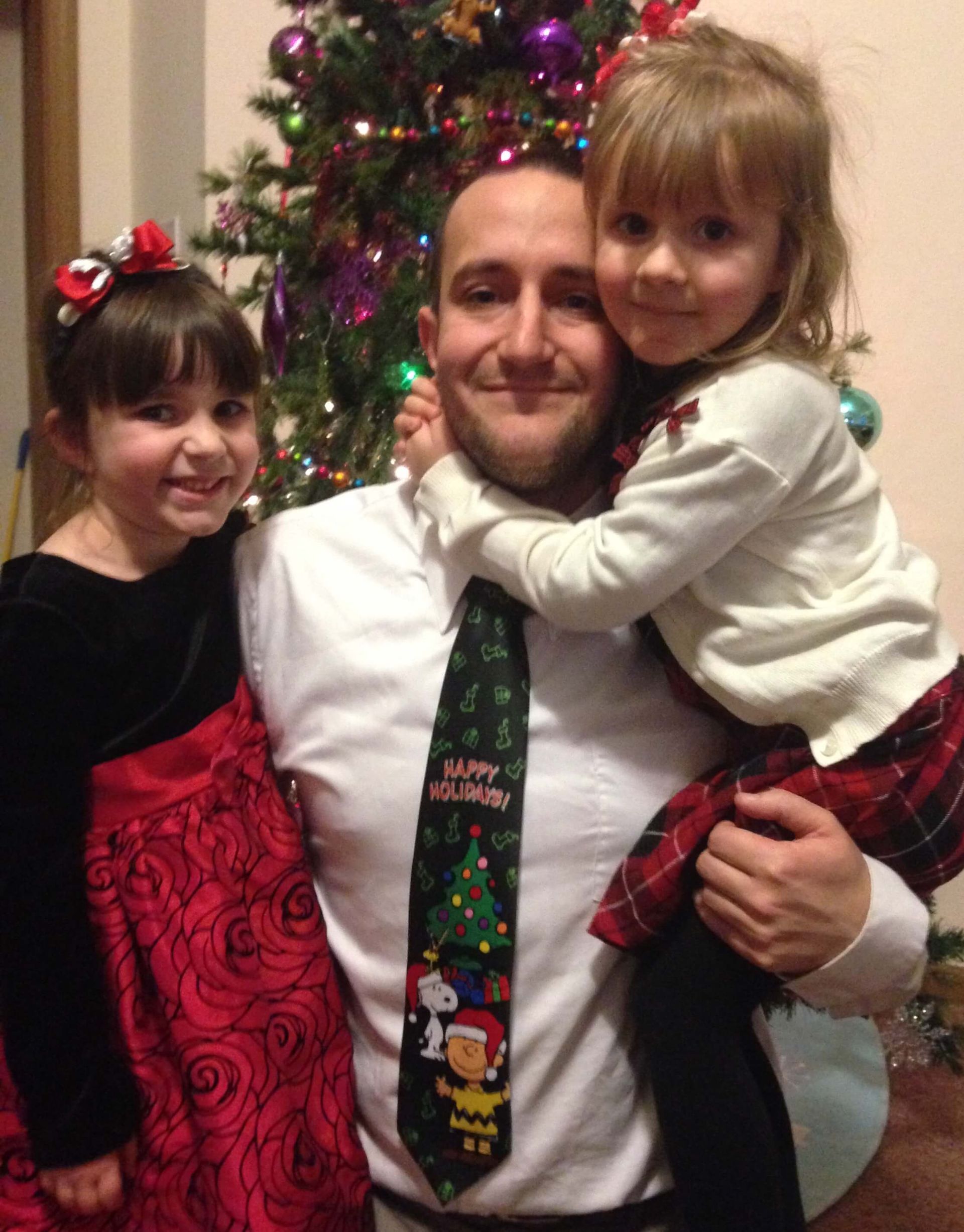 Man posing with two children in front of a decorated Christmas tree, all smiling.