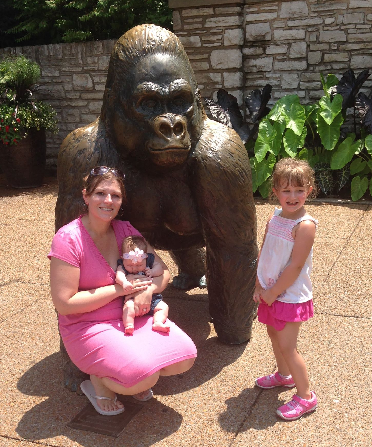 Holly with her child beside a gorilla statue while another child stands nearby in a garden setting