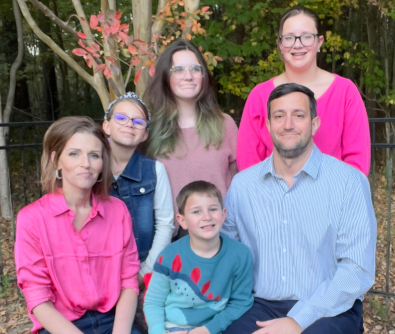 Group portrait of six people outdoors, smiling in front of flowering branches.