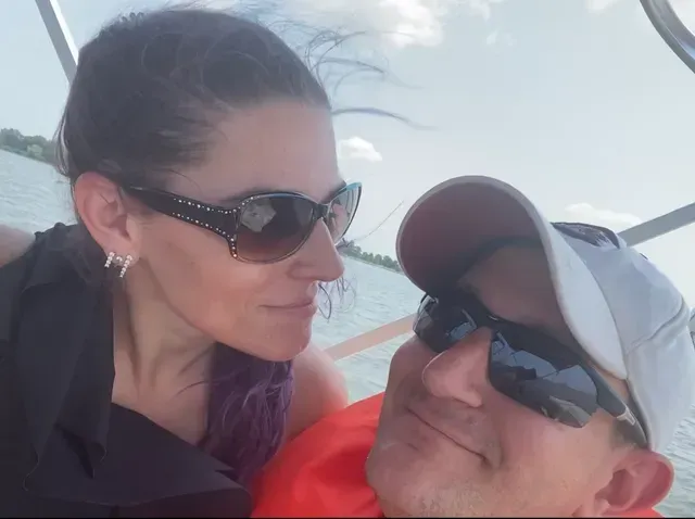Two people wearing sunglasses smiling on a boat with water in the background