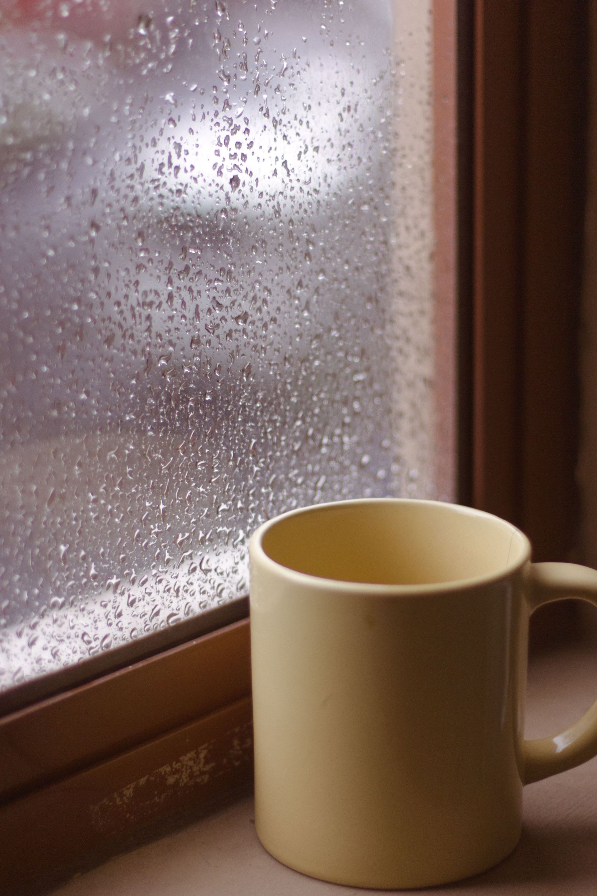 Cream mug by a rain-speckled window on a wooden sill