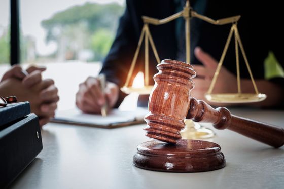 Gavel on sound block, scales of justice, person writing at table; legal setting.