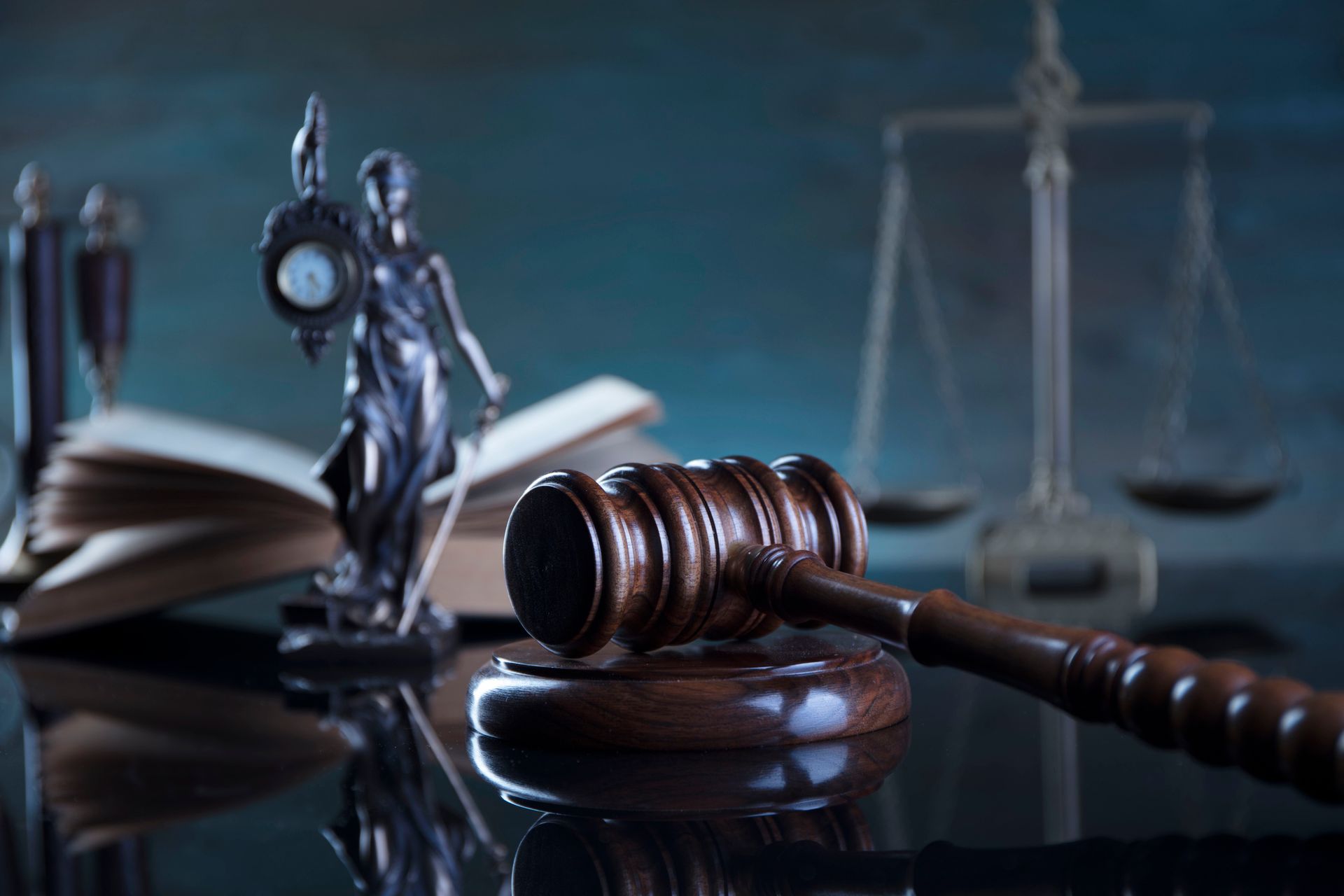 Gavel on a wooden block with scales, a statue of Lady Justice, and an open book in the background.