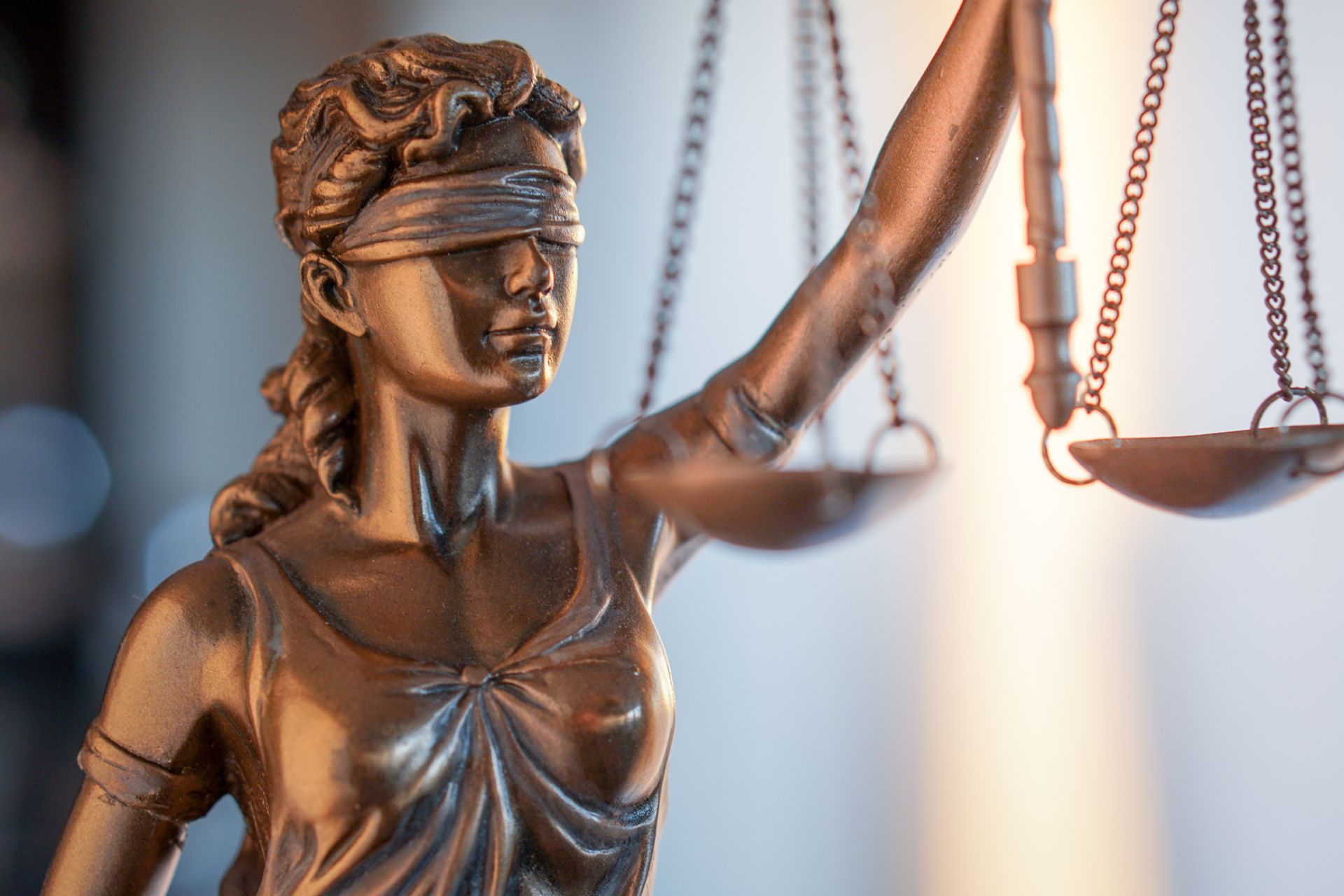 Bronze statue of Lady Justice wearing a blindfold and holding scales, set against a blurred background.
