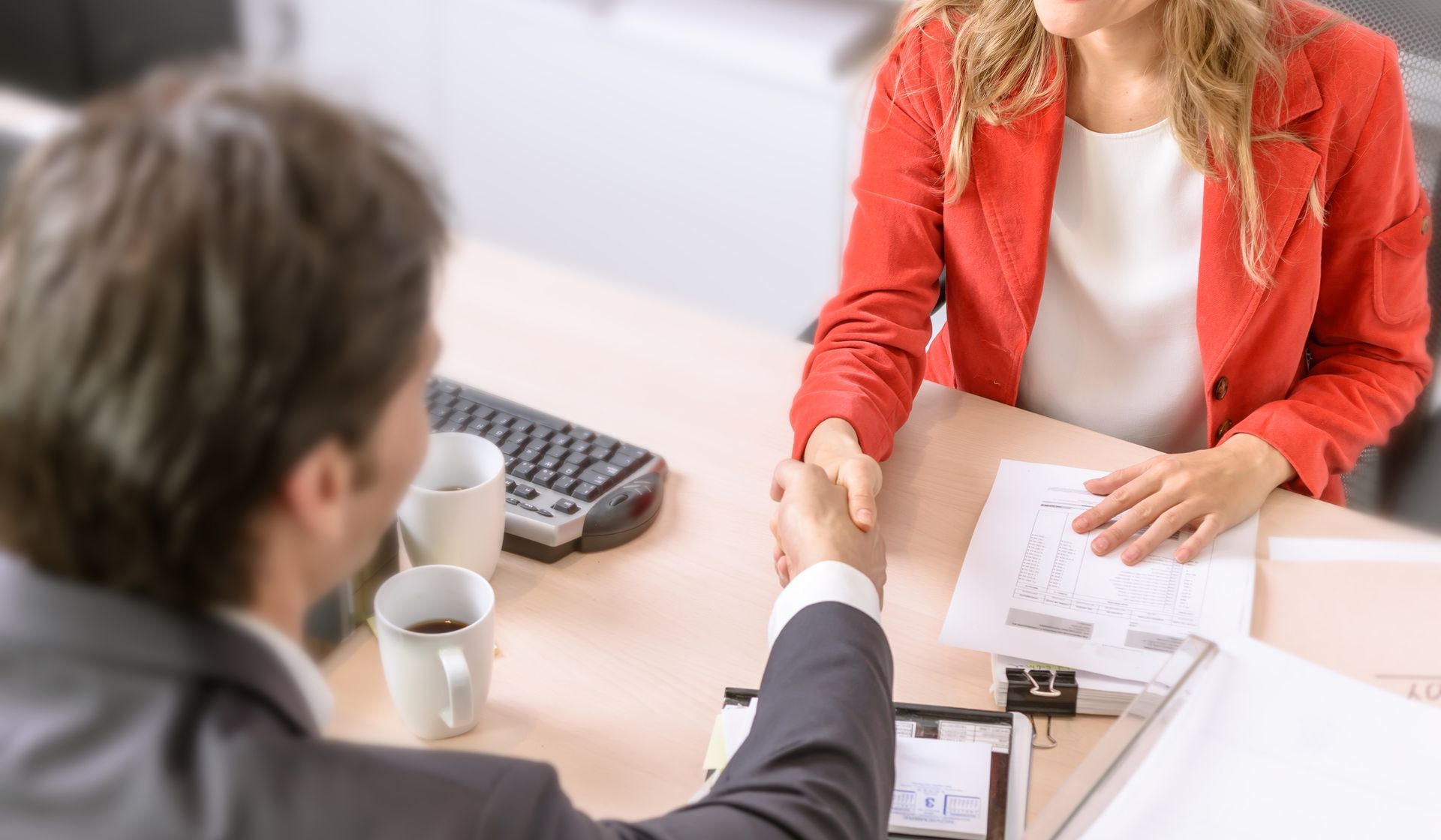 Two people shaking hands, miniature house, keys being handed over, document on a desk.