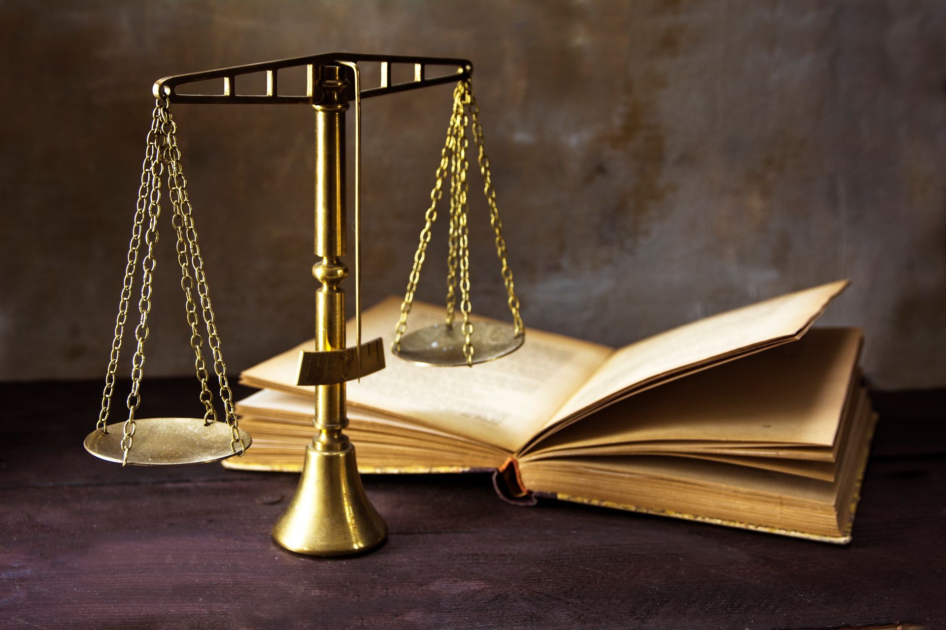 Gold justice scales next to an open, aged book on a dark surface.