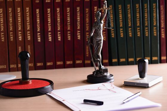 Statue of Lady Justice on desk with notary books and stamps.
