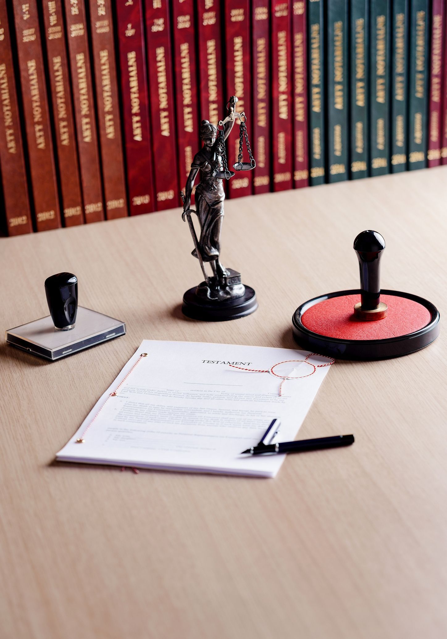 Legal documents and tools on a desk: books, Lady Justice statue, ink pads, and a pen.