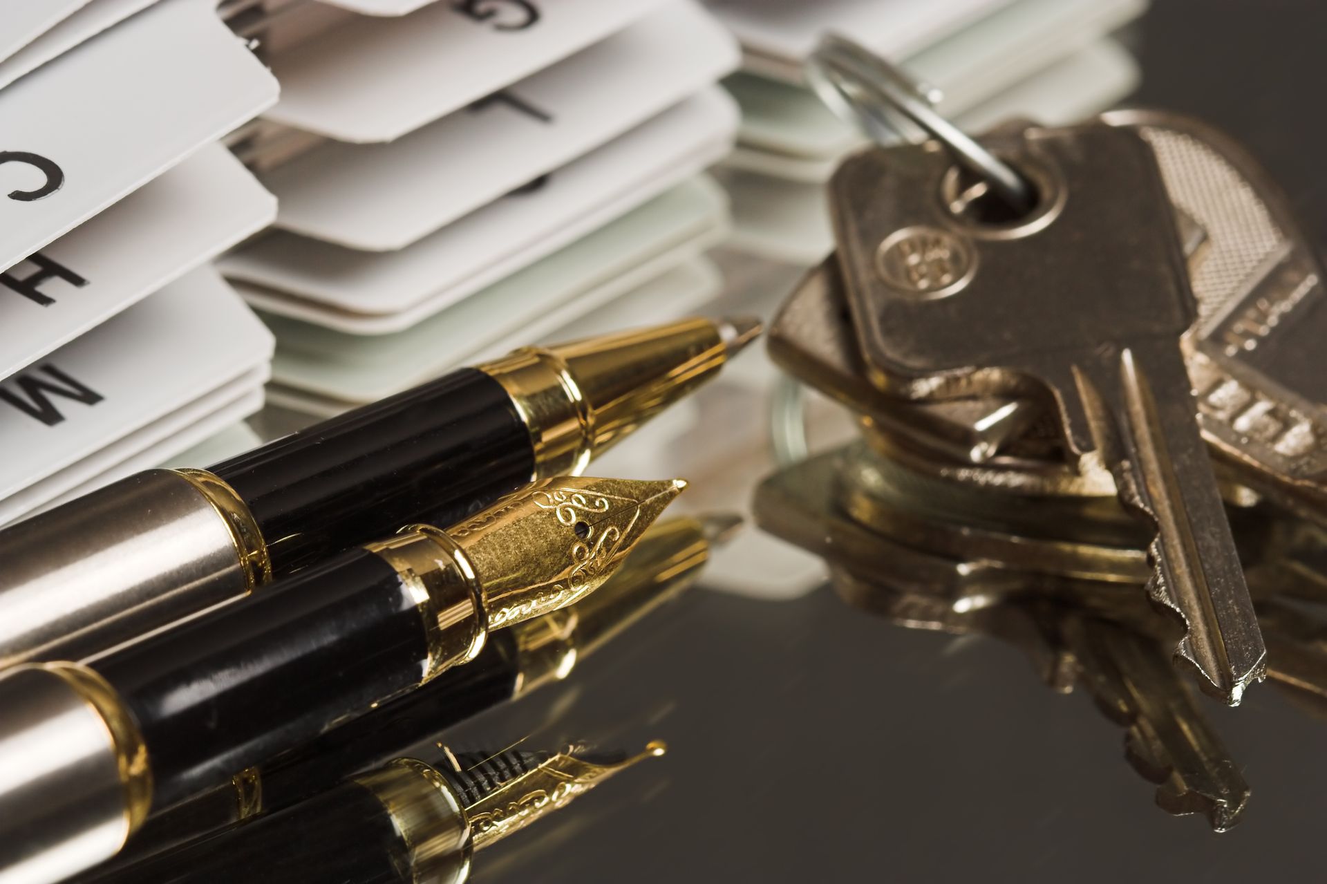 Pens, keys, and a stack of file cards on a reflective surface.