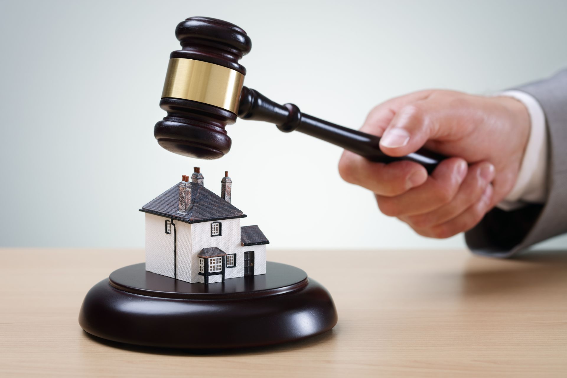 A gavel strikes a miniature house on a stand, symbolizing a real estate auction.