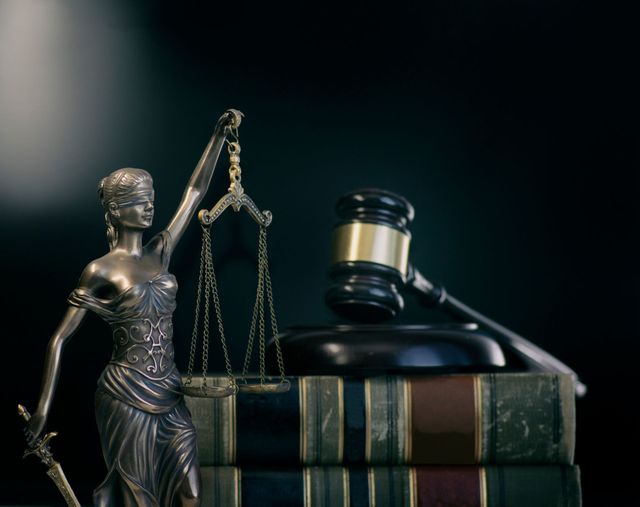 Statue of Lady Justice with scales, books, and gavel. Dark background.
