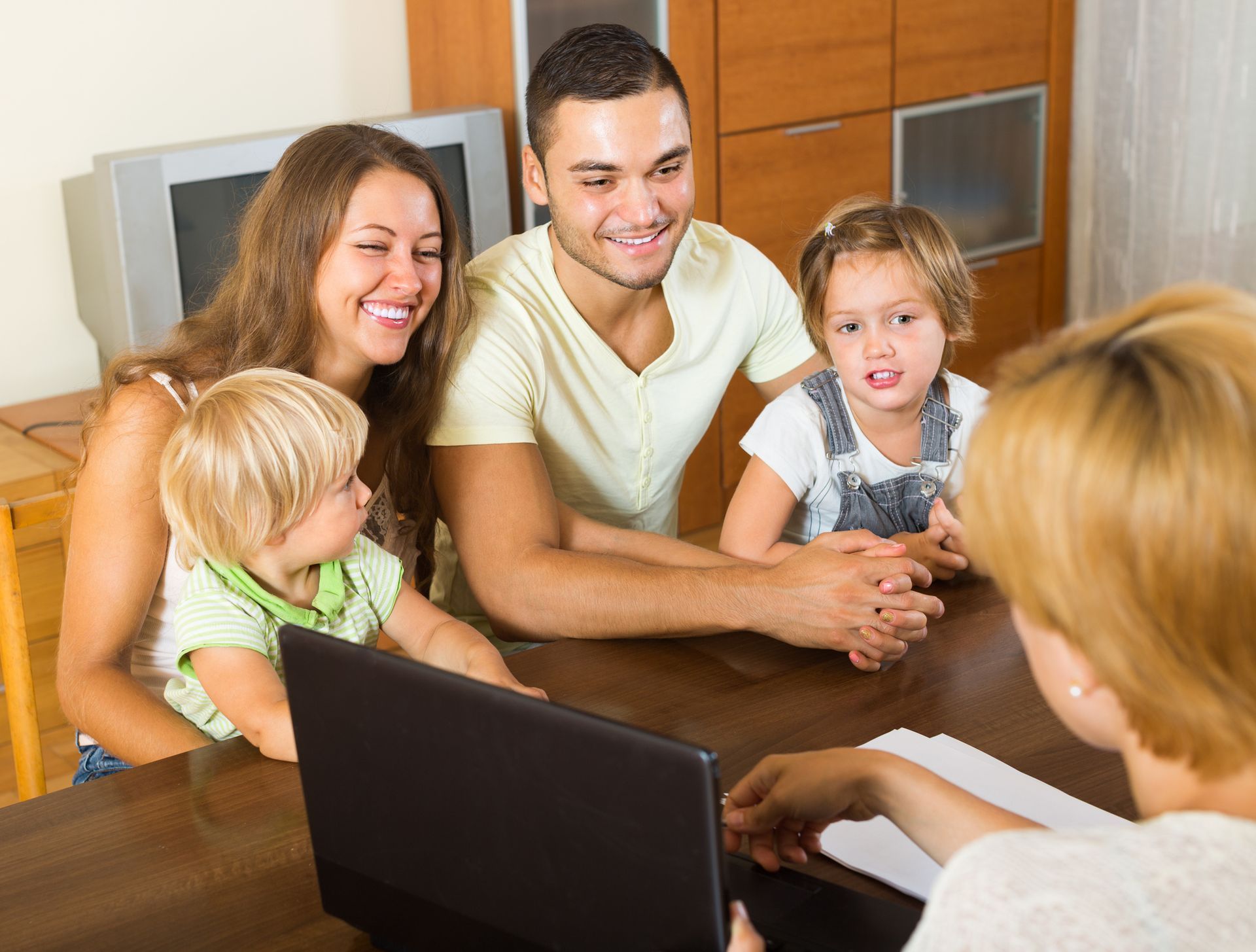 Family seated at a table with a person facing them, possibly a financial advisor, with laptop and papers present.