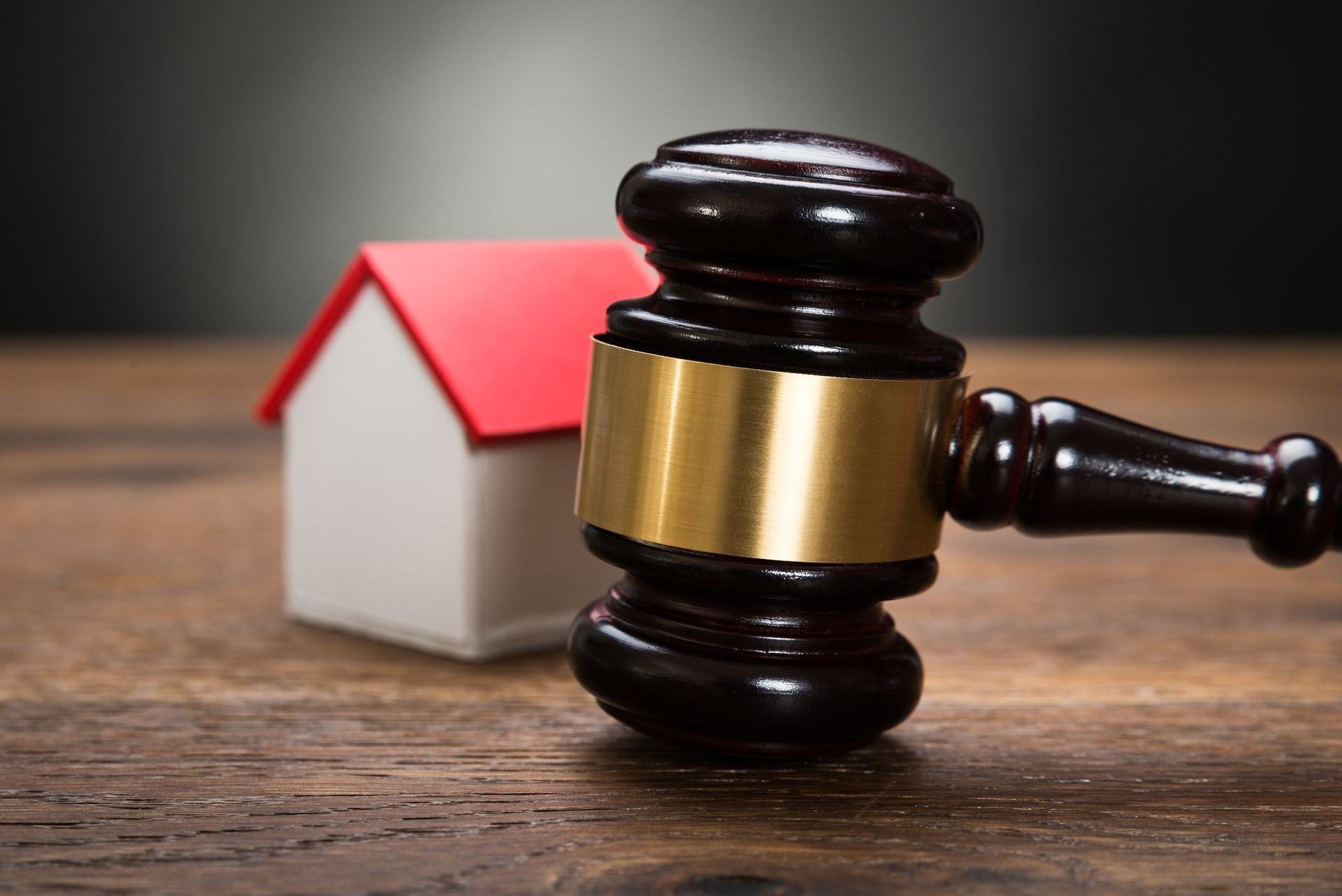 Wooden gavel striking a tabletop with a miniature house in the background.