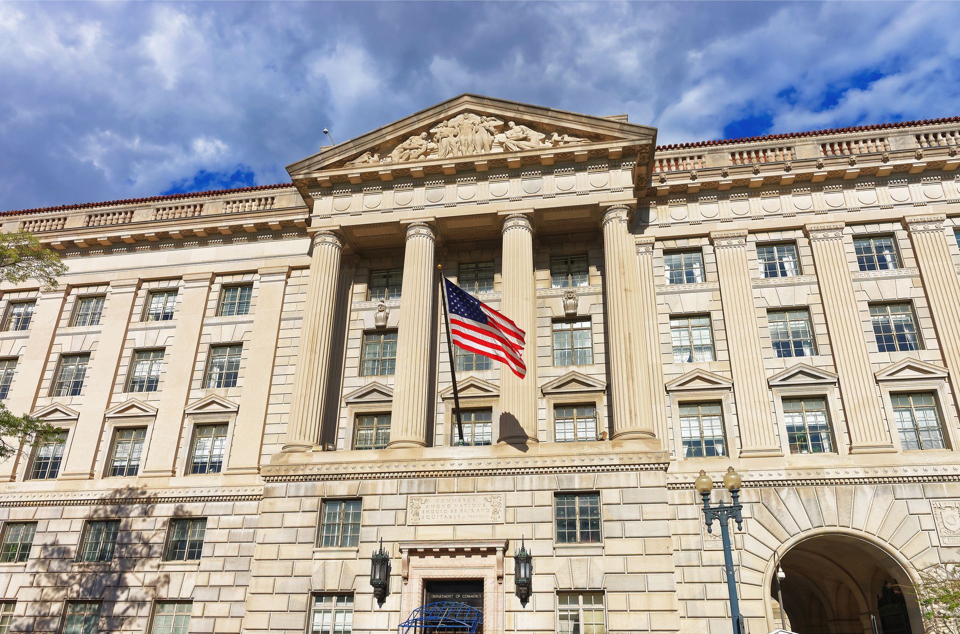 Government building facade with columns, American flag, and cloudy sky.