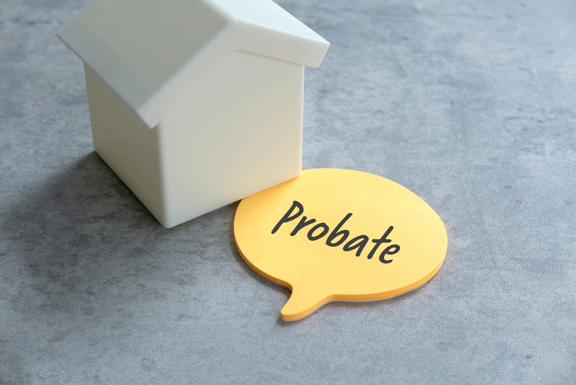 A white toy house next to a yellow speech bubble with the word  Probate. Gray surface.