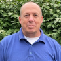 Man in blue polo shirt against green foliage.