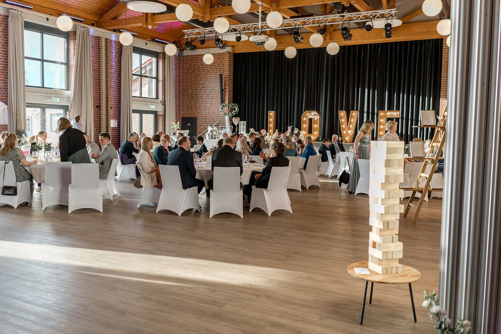 Ein großer Raum mit Tischen und Stühlen, aufgestellt für einen Hochzeitsempfang.