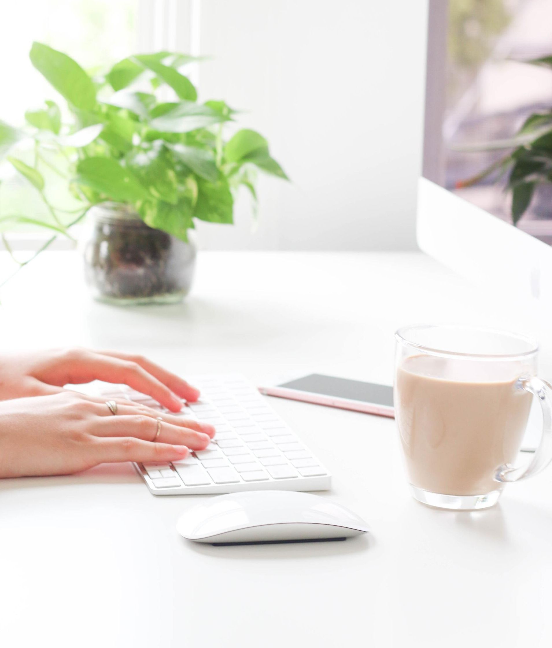 A person is typing on a keyboard next to a cup of coffee.
