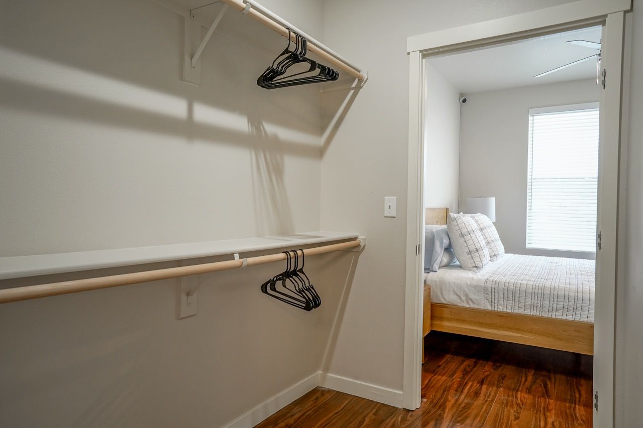 Walk-in closet with two hanging rods and empty shelves, opening into a bedroom.