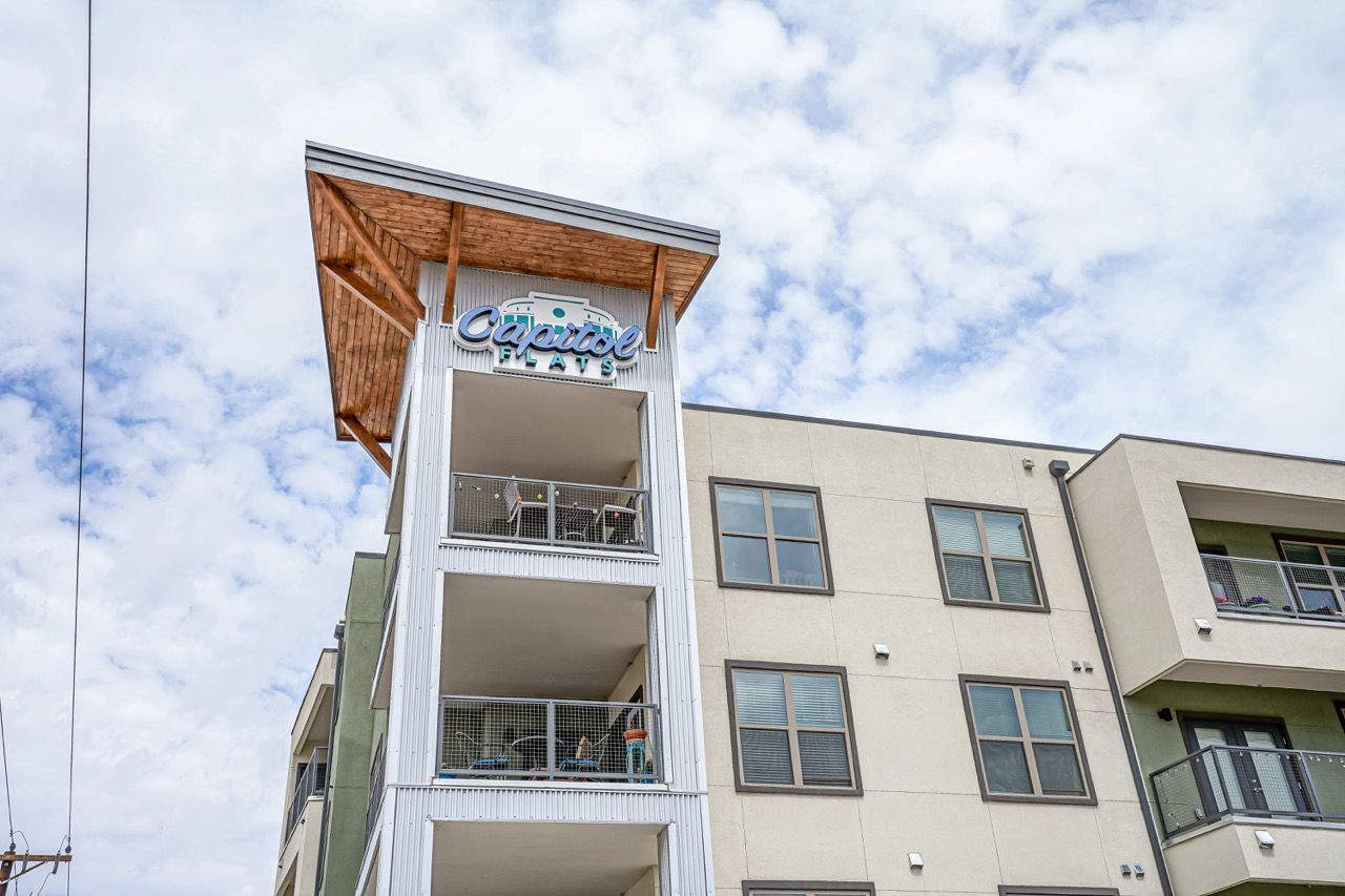 Exterior view of a modern apartment building with balconies and a Capitol sign under a cloudy sky.