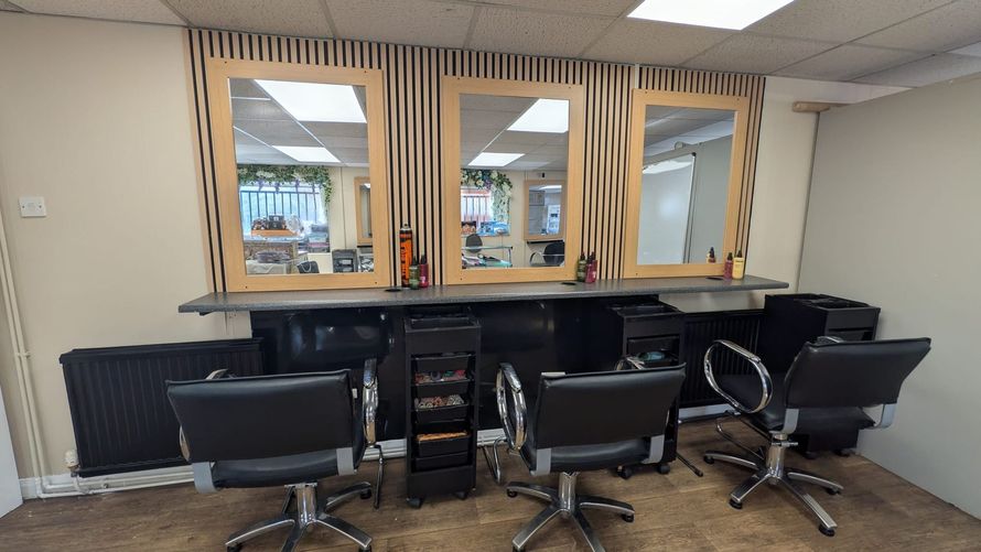 Salon workstation with two black styling chairs, large mirrors, and shelves against a beige wall