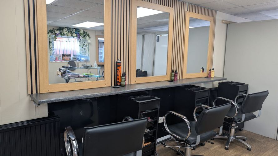 Salon waiting area with black chairs and large wall mirrors beneath wooden cabinets