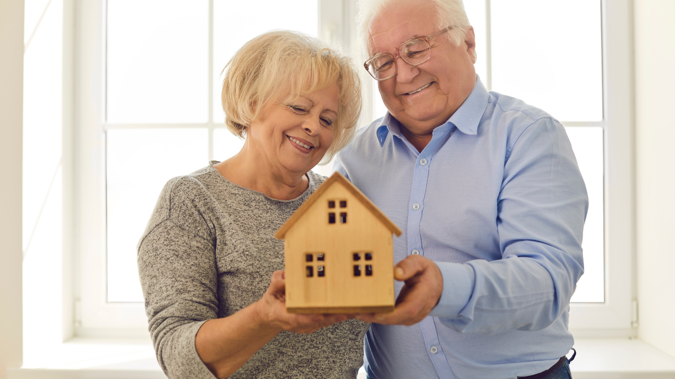 Smiling older couple holding a small house model indoors