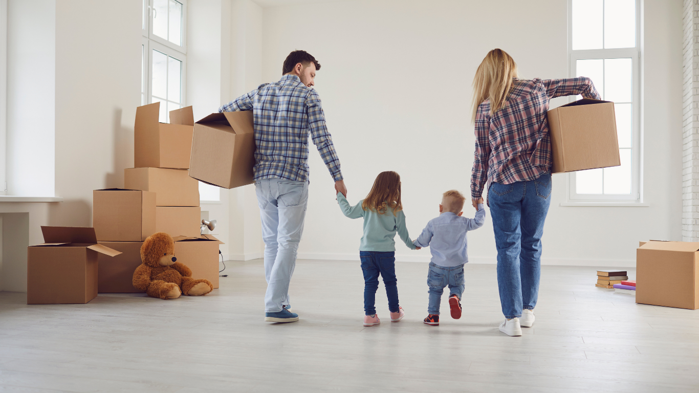 Family carrying boxes into a bright, empty room during a move