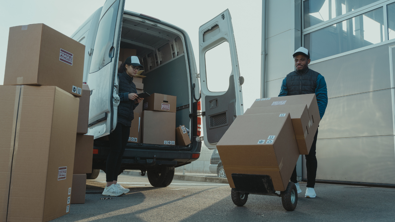 Workers loading cardboard boxes into a white delivery van in an industrial yard
