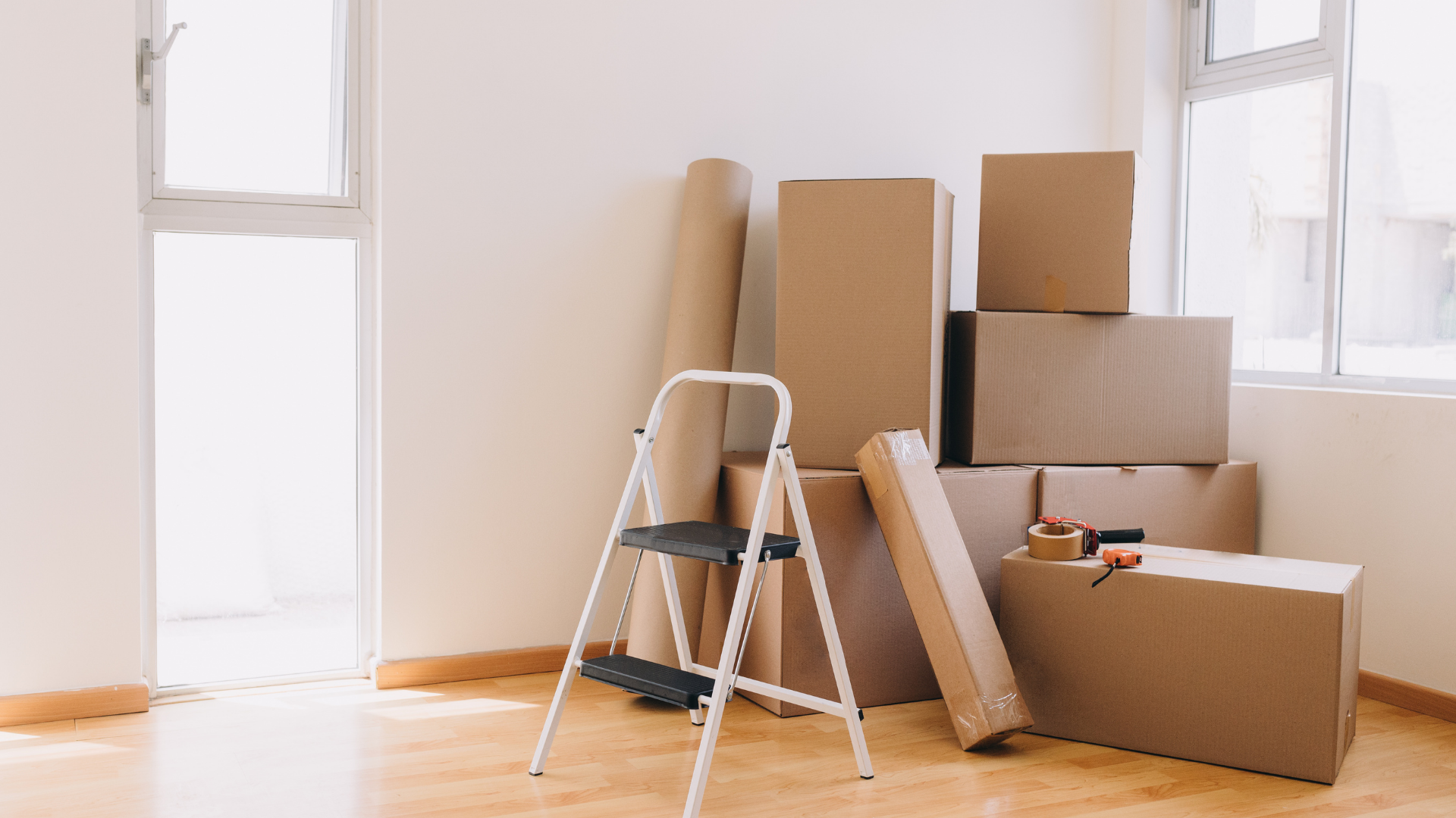 Room with cardboard moving boxes, rolled paper, small step ladder, and tools.
